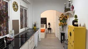 Een moderne keuken met een zwart aanrecht, een spoelbak en een wasmachine. Er is een geel kastje met een decoratief object erboven.