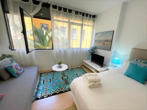 Une chambre d’hôtel avec un lit, une télévision, une petite table avec une plante et une fenêtre avec des rideaux.