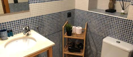 A bathroom with a white sink, a toilet, and a shelf with toiletries.