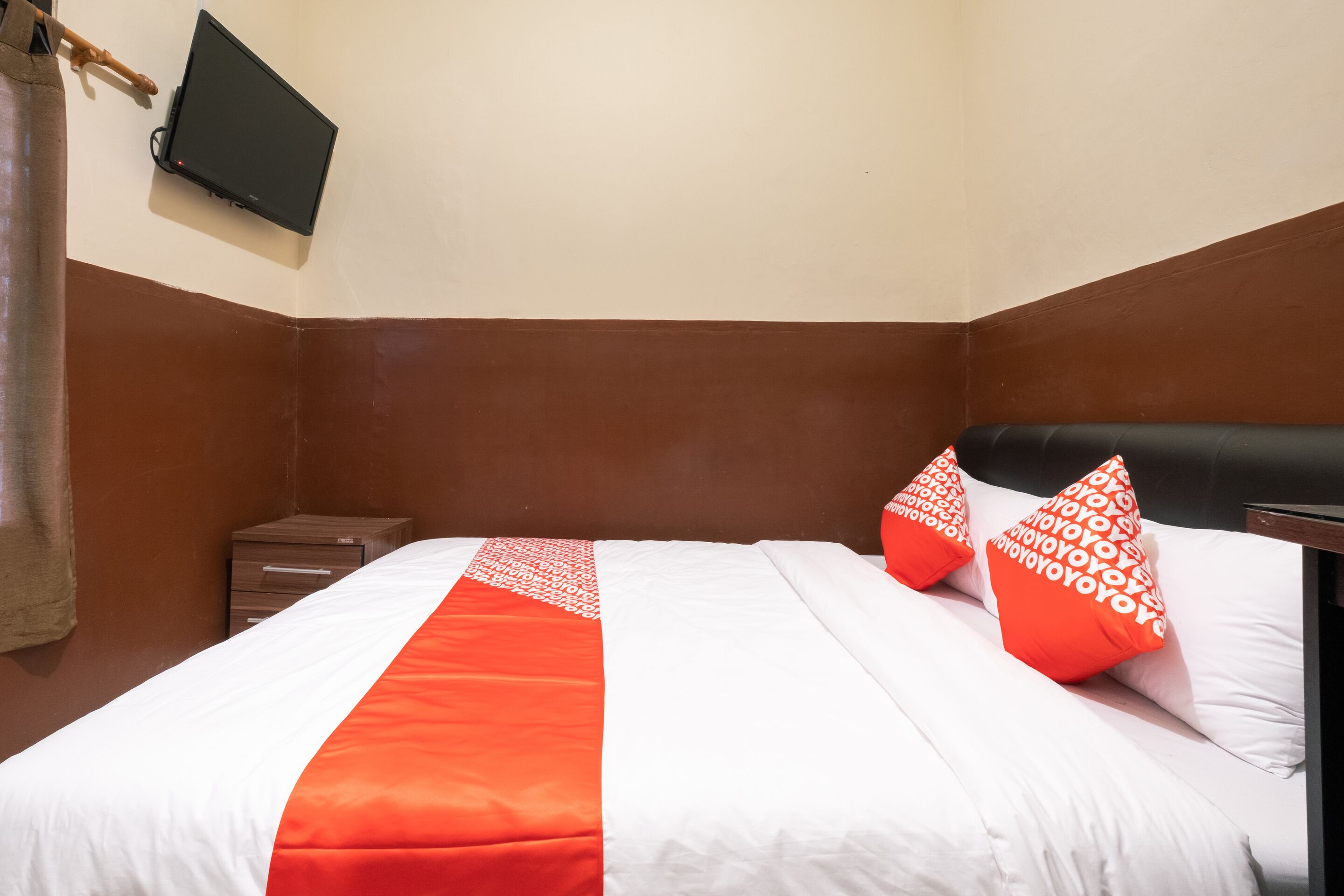 A neatly made bed with white and orange bedding, a small bedside table, and a wall-mounted TV.