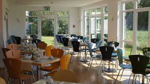 Un comedor con mesas y sillas, ventanas amplias y vistas al exterior.