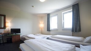 Una habitación de hotel con dos camas individuales, un escritorio con televisor y dos lámparas de noche.