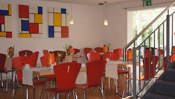 A dining area with red chairs and tables, a staircase, and abstract wall art.