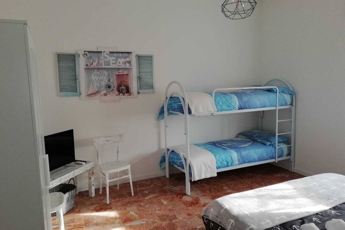 A room with bunk beds, a desk with a chair, and a television.