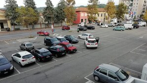 A parking lot with various cars, a pedestrian crossing, and buildings in the background. - Good Morning Shopping (Serravalle Scrivia)