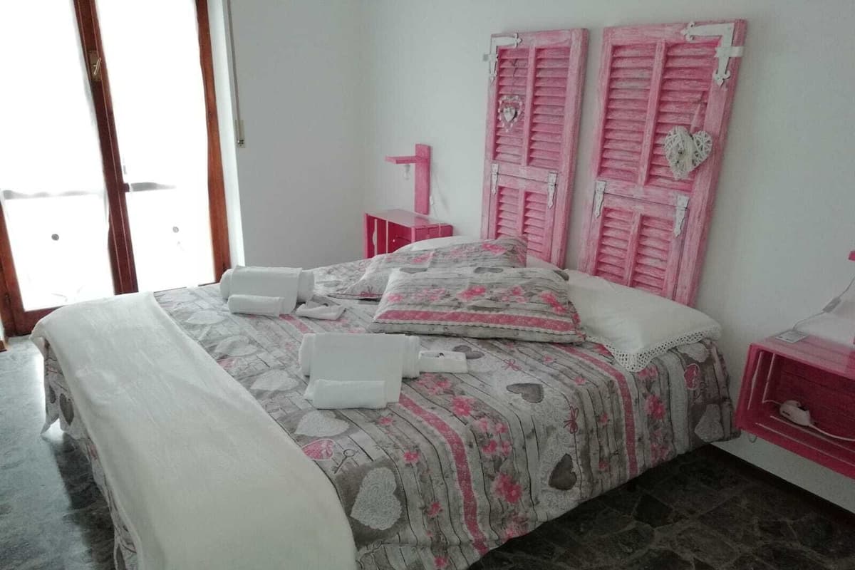 A bed with pink shutters, a bedside table, and a lamp.