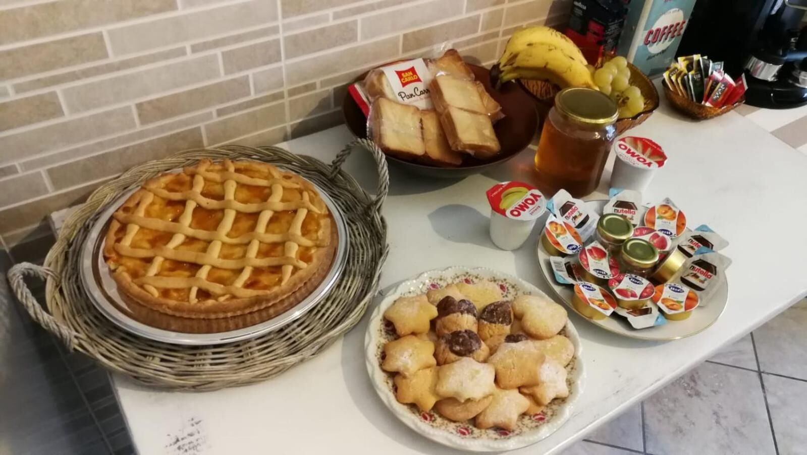 A table with a pie, bread, bananas, honey, and Nutella jars.