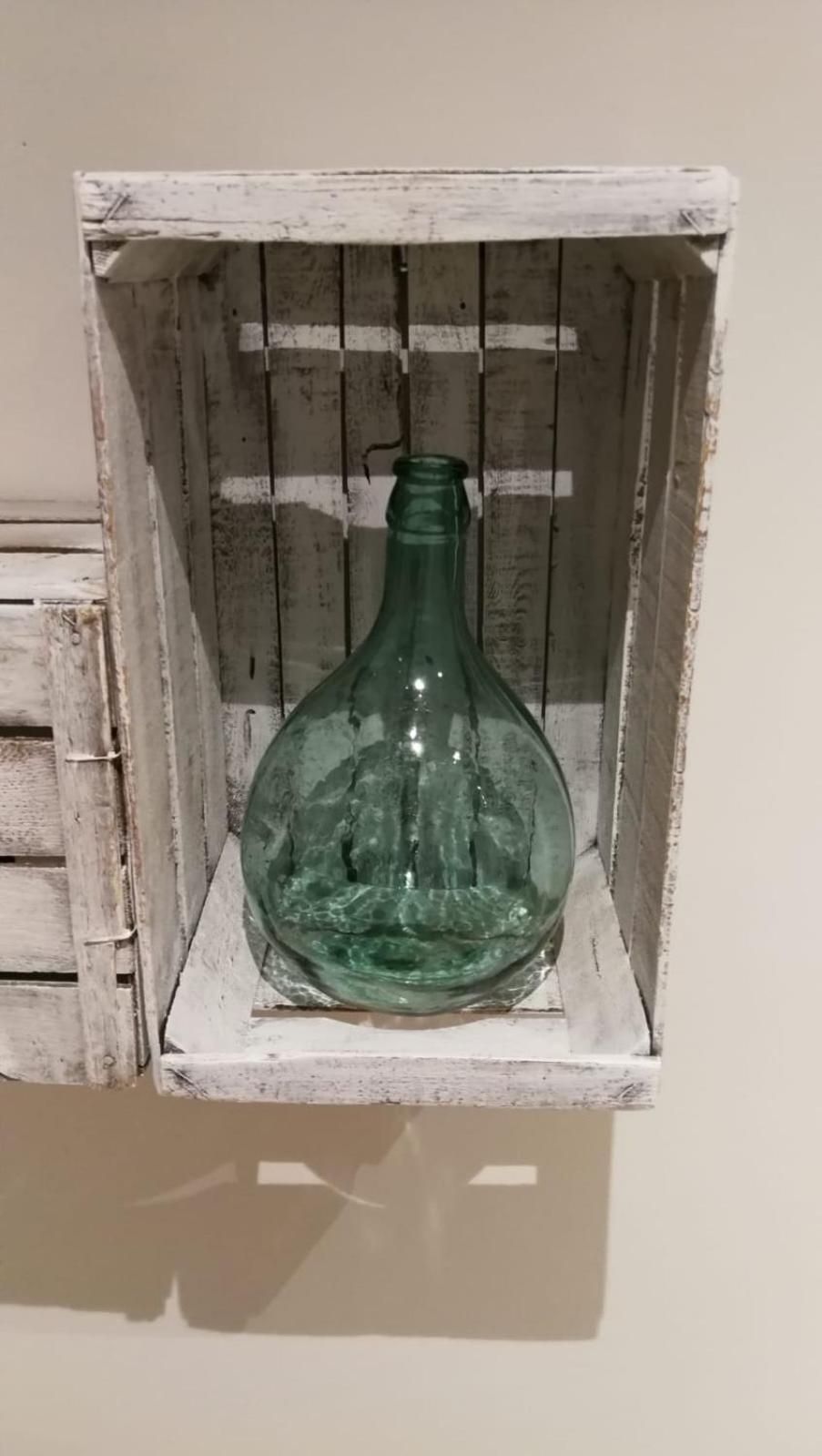 Een groene glazen fles in een houten kist met een rustieke uitstraling.