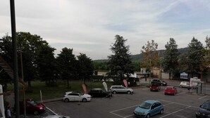 A parking lot with multiple cars and a few pedestrians. - Good Morning Shopping (Serravalle Scrivia)