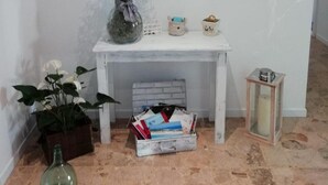 A white console table with a vase of white flowers, a small potted plant, a mirror, and a box of books. - Good Morning Shopping (Serravalle Scrivia)