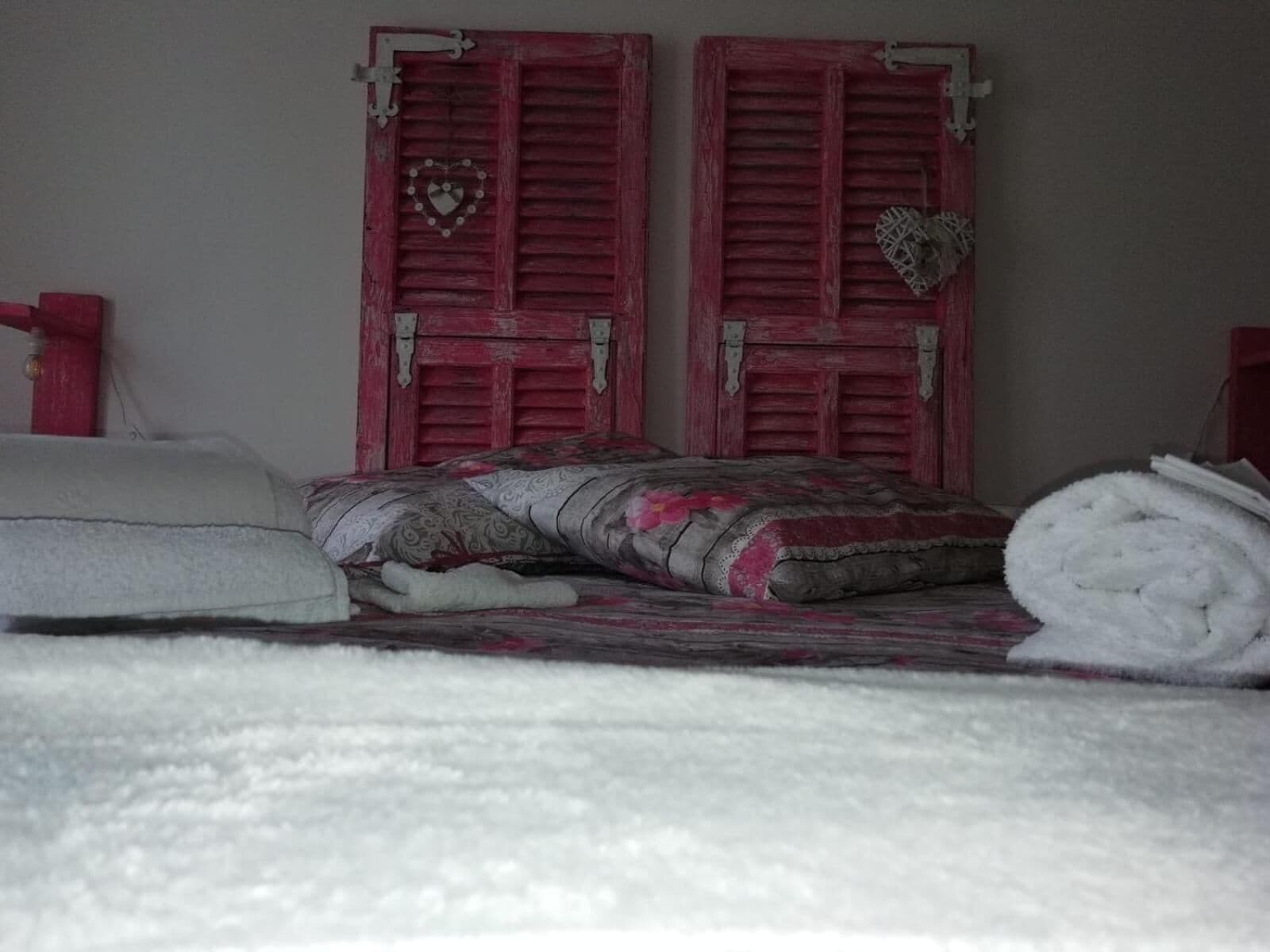Un lit avec une couverture à motifs et des oreillers, une serviette blanche enroulée et deux portes rouges décorées de motifs en forme de cœur.