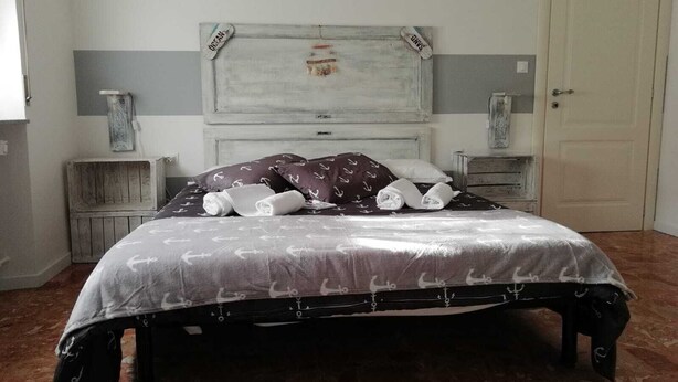 A bed with a patterned bedspread, two nightstands, a wooden headboard, and a door in the background. - Good Morning Shopping (Serravalle Scrivia)