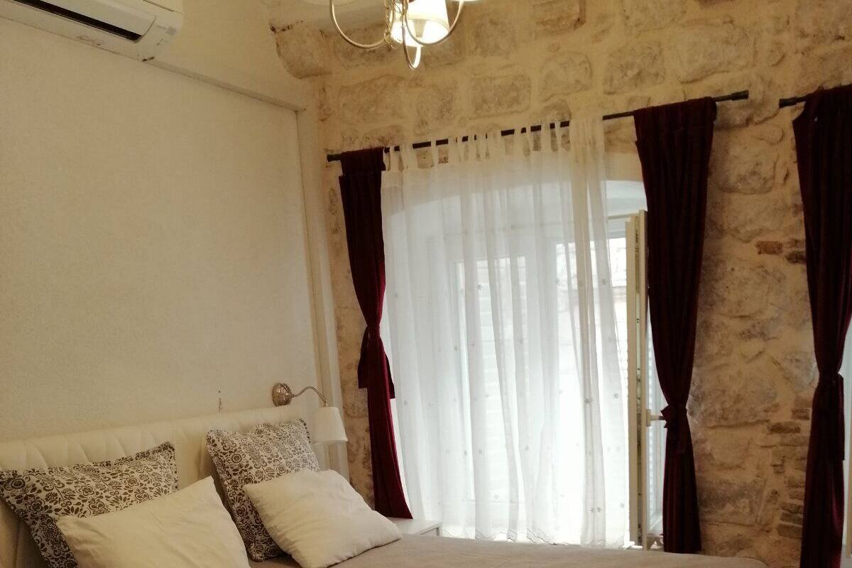 A bedroom with a large bed, stone walls, and a window with curtains.