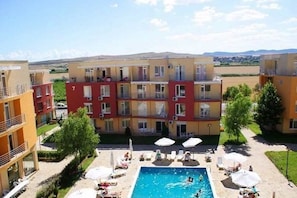 A multi-story hotel with a swimming pool, outdoor seating, and a view of the surrounding landscape. - Sunny Day 5 Menada Apartments (Nessebar)