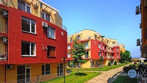 Una hilera de edificios residenciales de varios pisos con balcones, un sendero pavimentado y una pequeña zona verde.