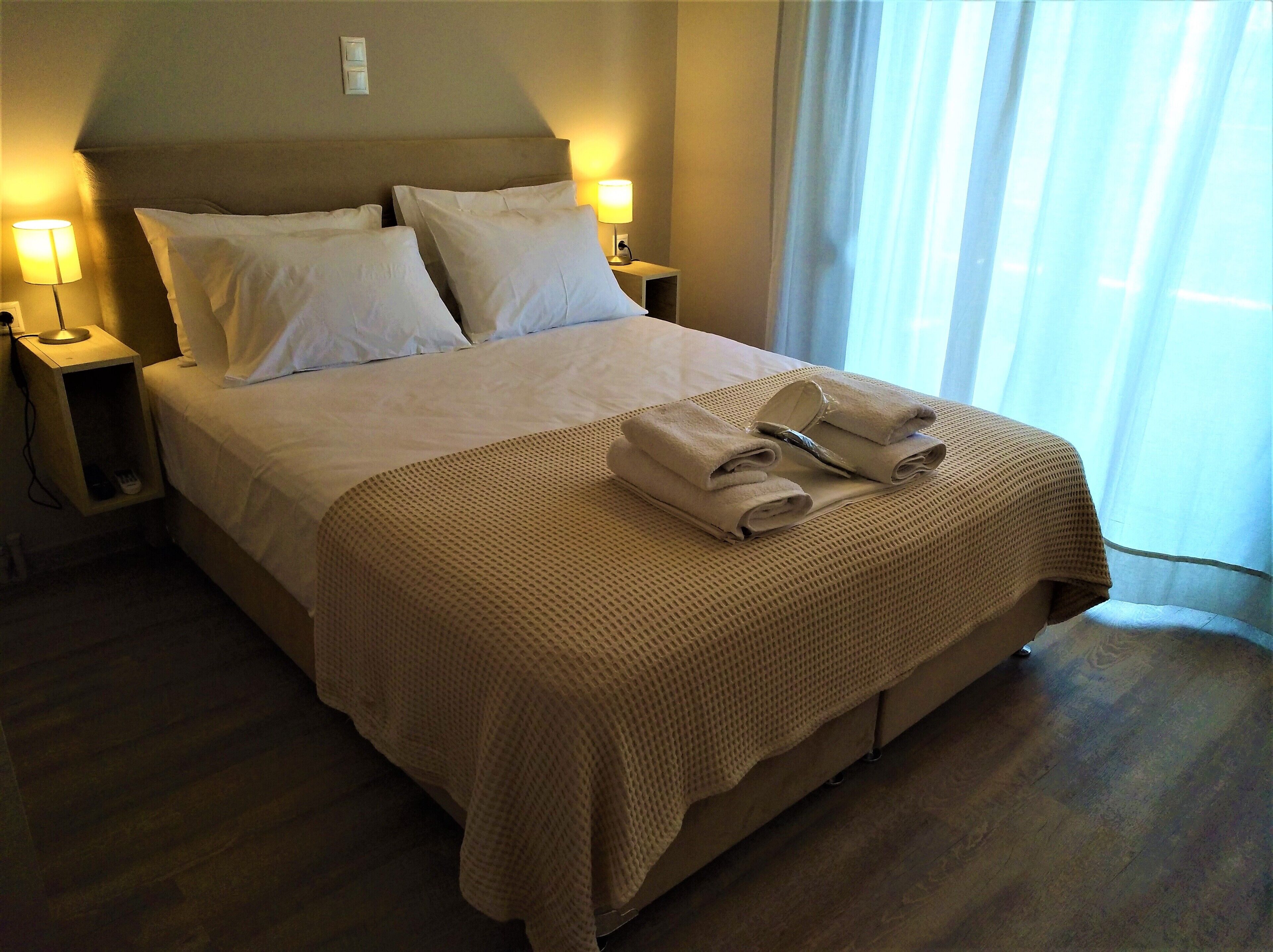 A neatly made bed with a beige bedspread and pillows, two bedside lamps, and a folded towel on the bed.