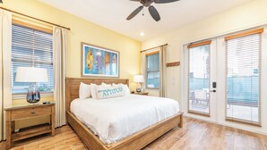 A bedroom with a wooden bed, two bedside tables with lamps, a ceiling fan, and a painting on the wall.