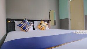 Una cama con una colcha azul y blanca, dos almohadillas decorativas con patrones geométricos, un cabecero de madera y un espejo en la pared.