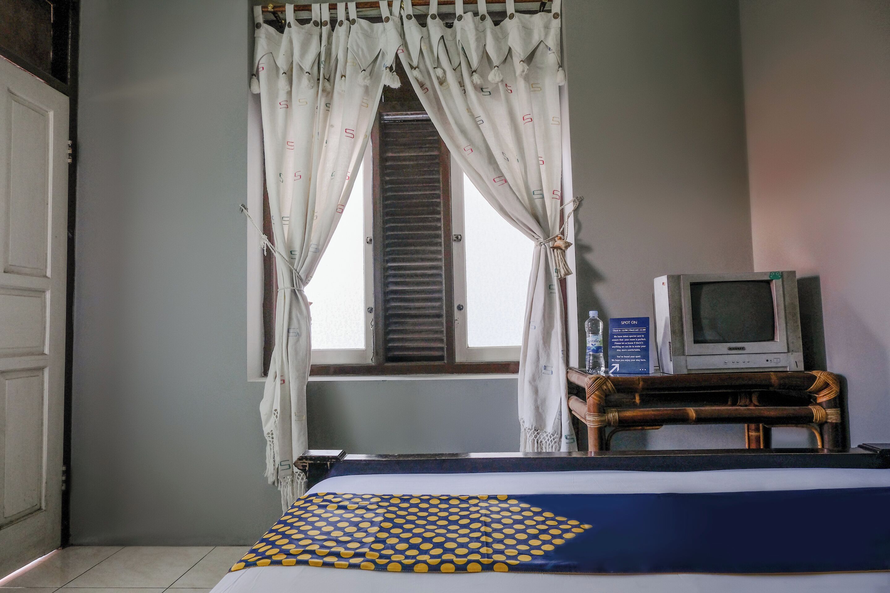 Una habitación con una cama, un televisor sobre un mueble de madera y una ventana con cortinas.