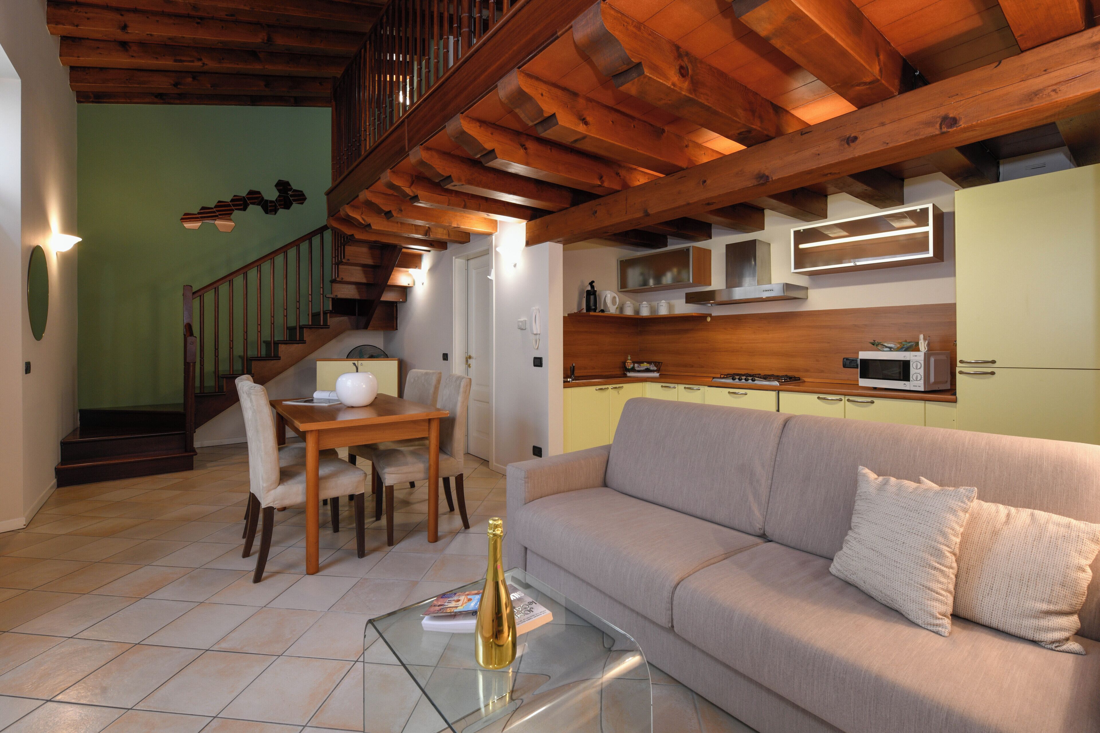 Un salon comprenant un canapé, une table basse en verre, une table à manger avec des chaises, un escalier et des poutres en bois au plafond.