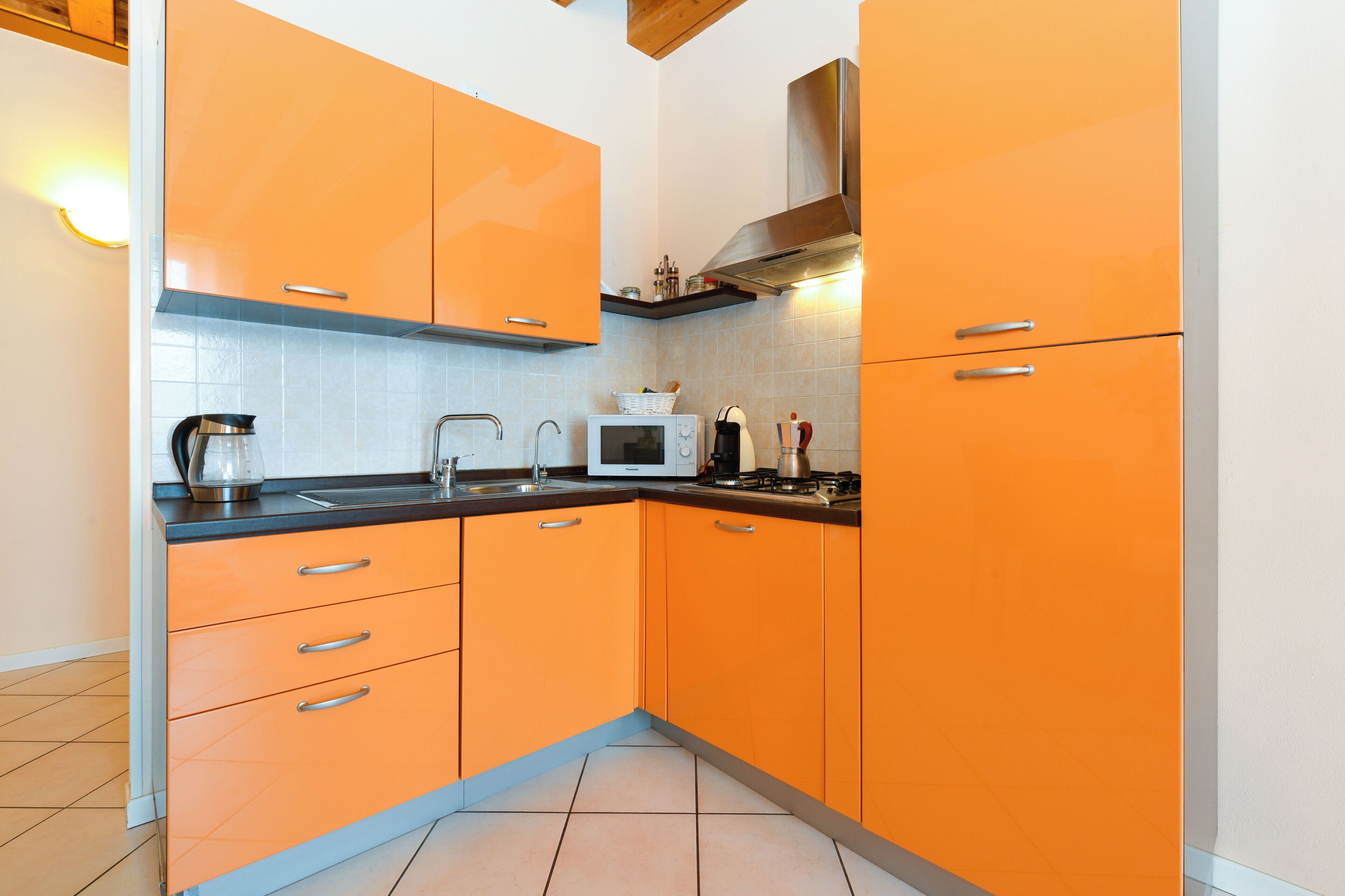 Una cocina con armarios color naranja, un microondas, un hervidor y un lavabo.