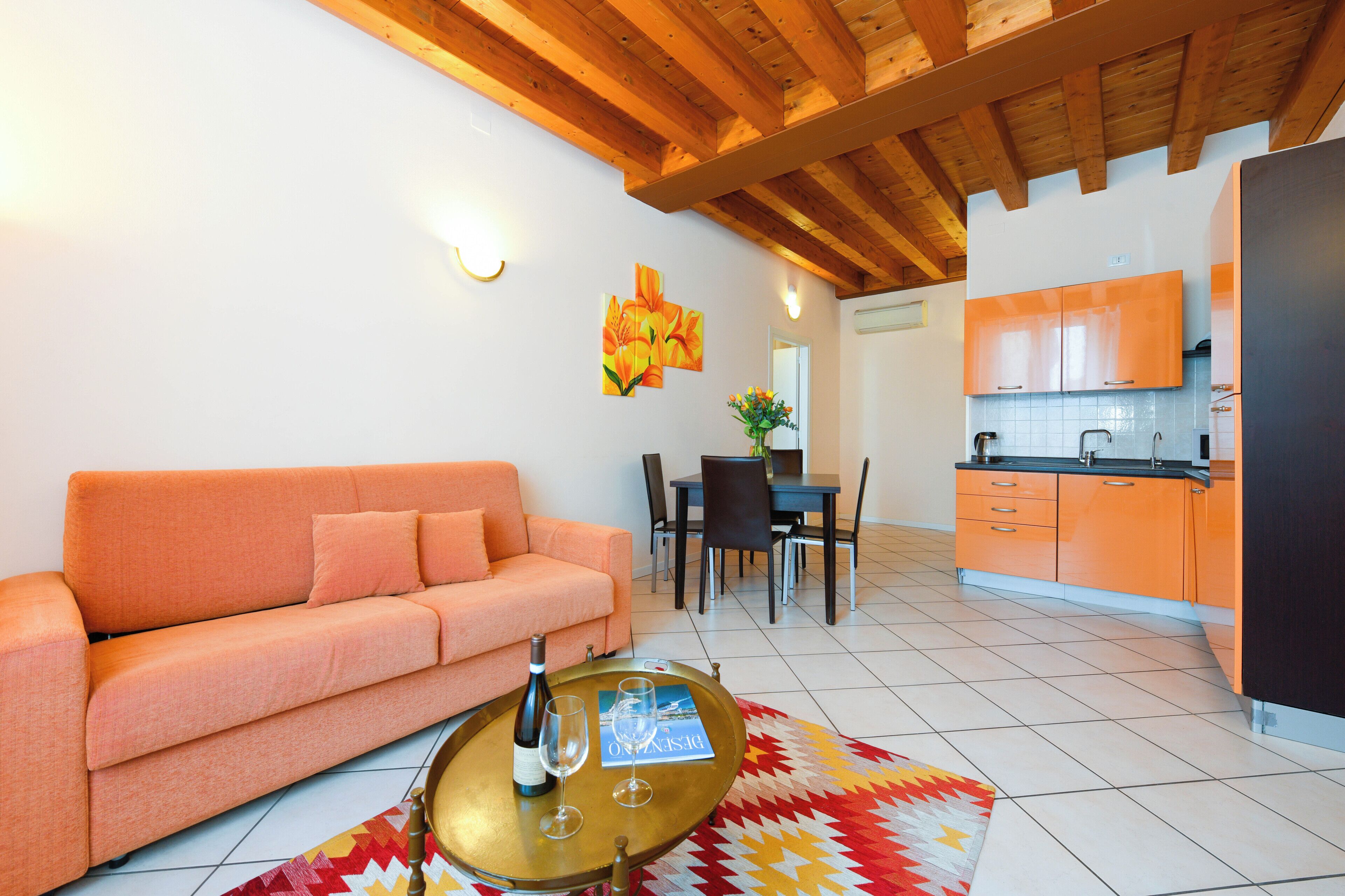 A living room with a sofa, a dining table with chairs, and a kitchen area with orange cabinets.