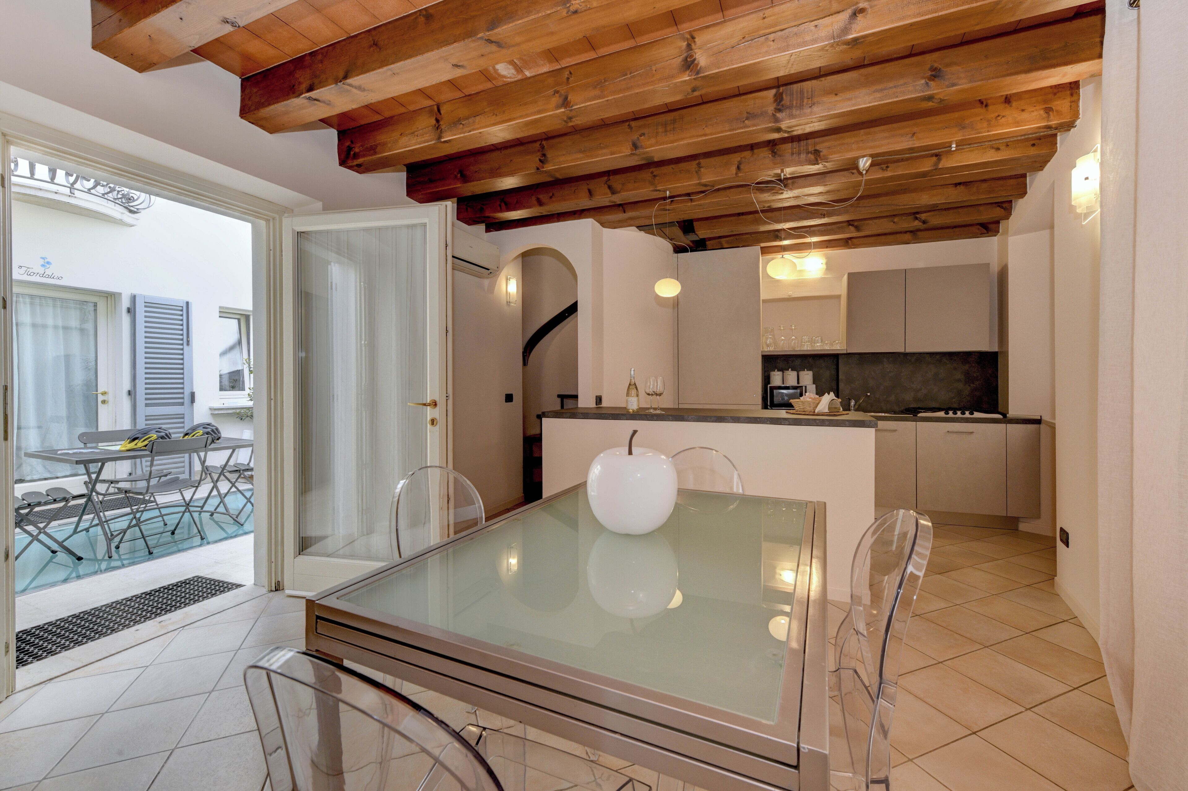 A modern kitchen with wooden beams, a glass dining table, and a view of a pool outside.