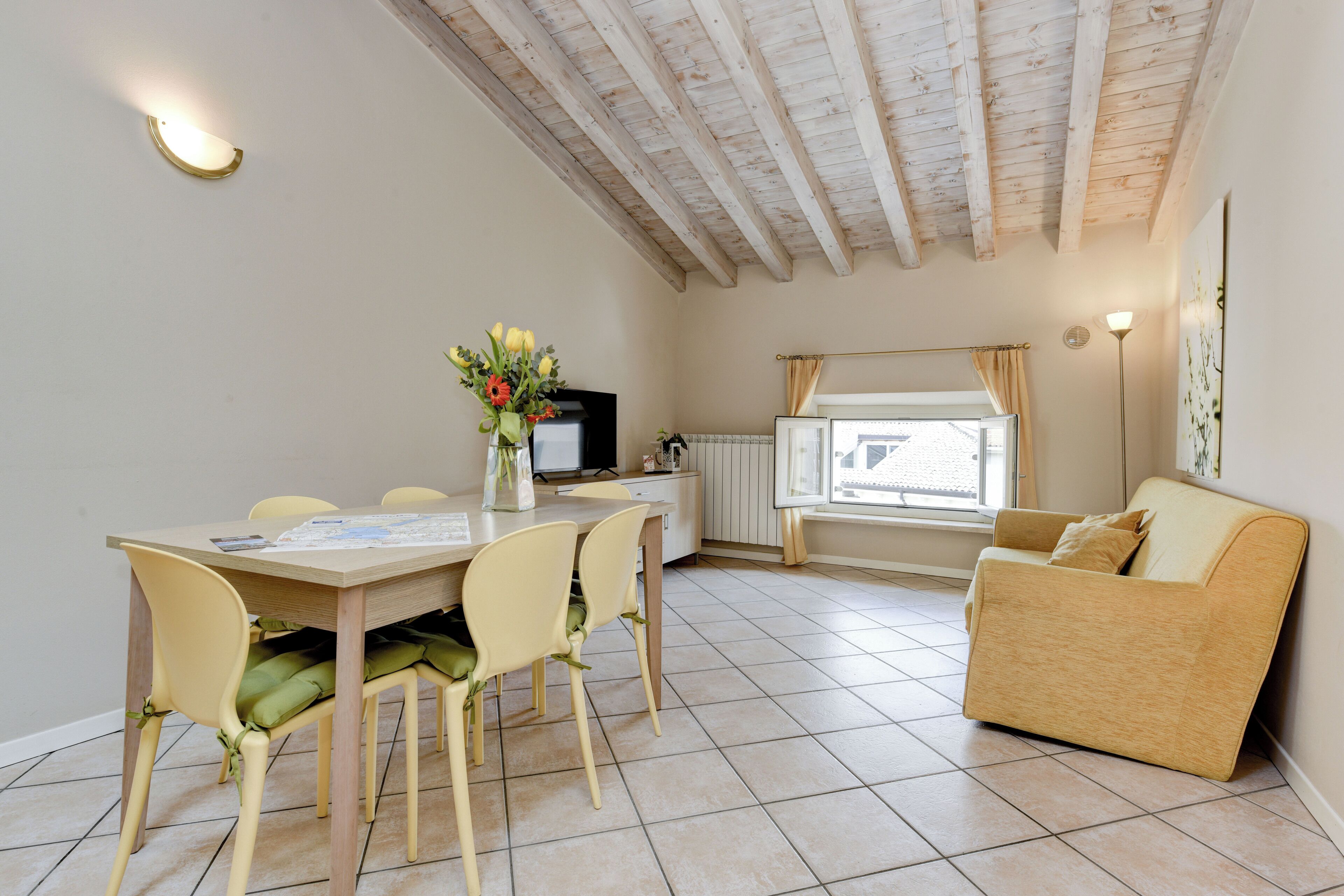 A dining area with a wooden table and chairs, a TV, and a window with curtains.
