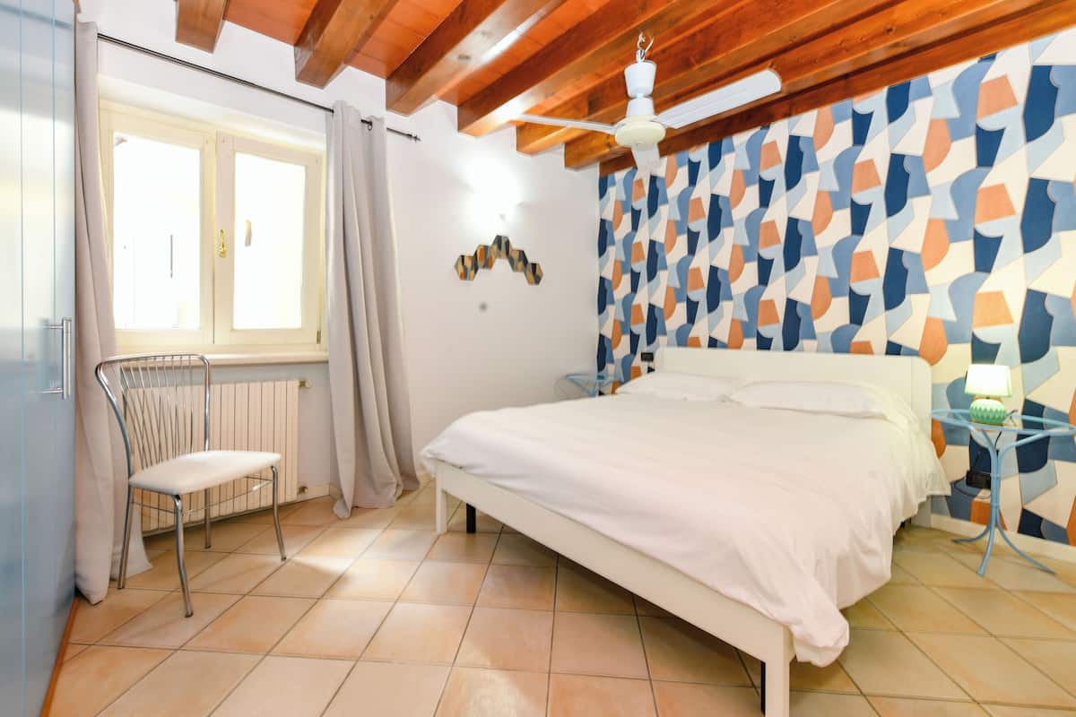 Ein Schlafzimmer mit einem Bett, einem Sessel, einer Heizung, einem Deckenventilator und einer Wand mit Muster.
