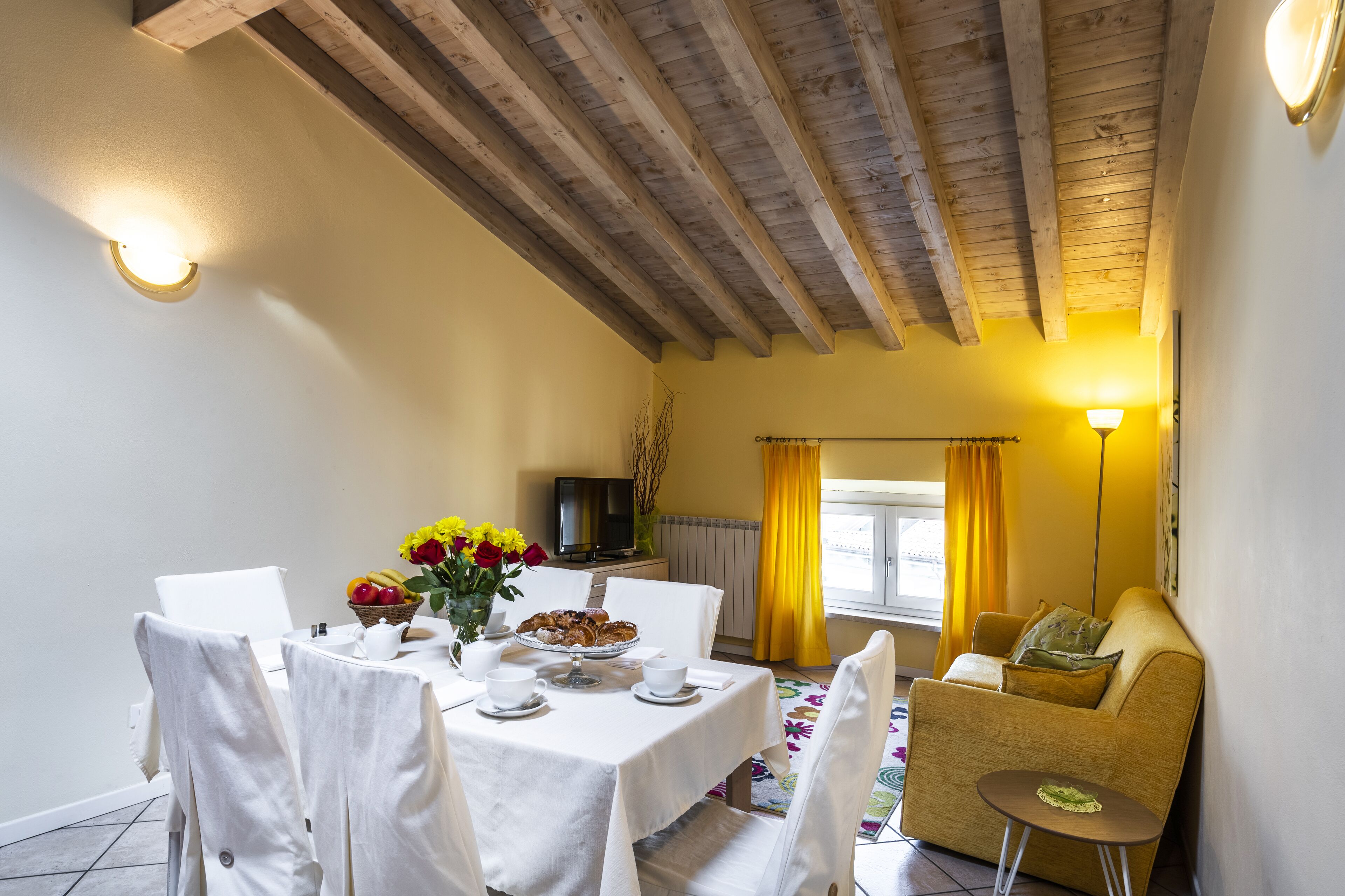 A dining area with a table set for breakfast, a sofa, and a TV in the background.
