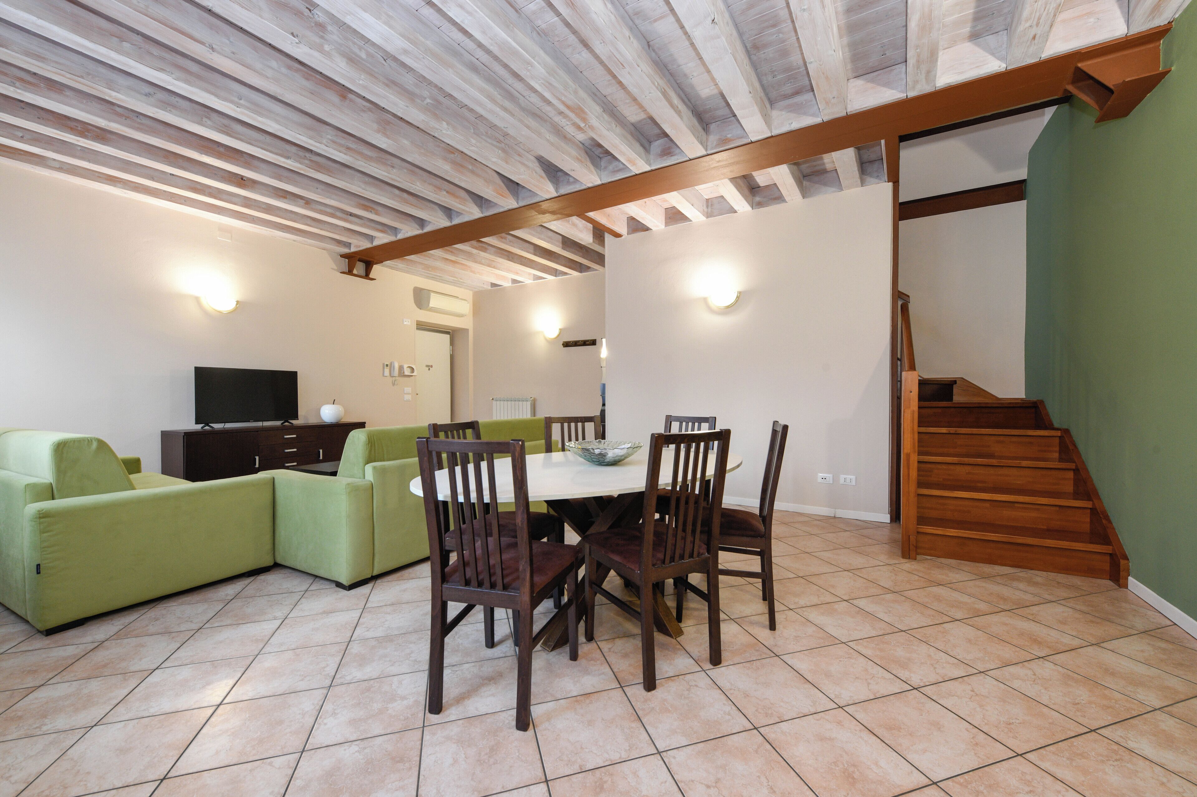 Un área de comedor con una mesa y sillas, un sofá verde, un televisor y una escalera.
