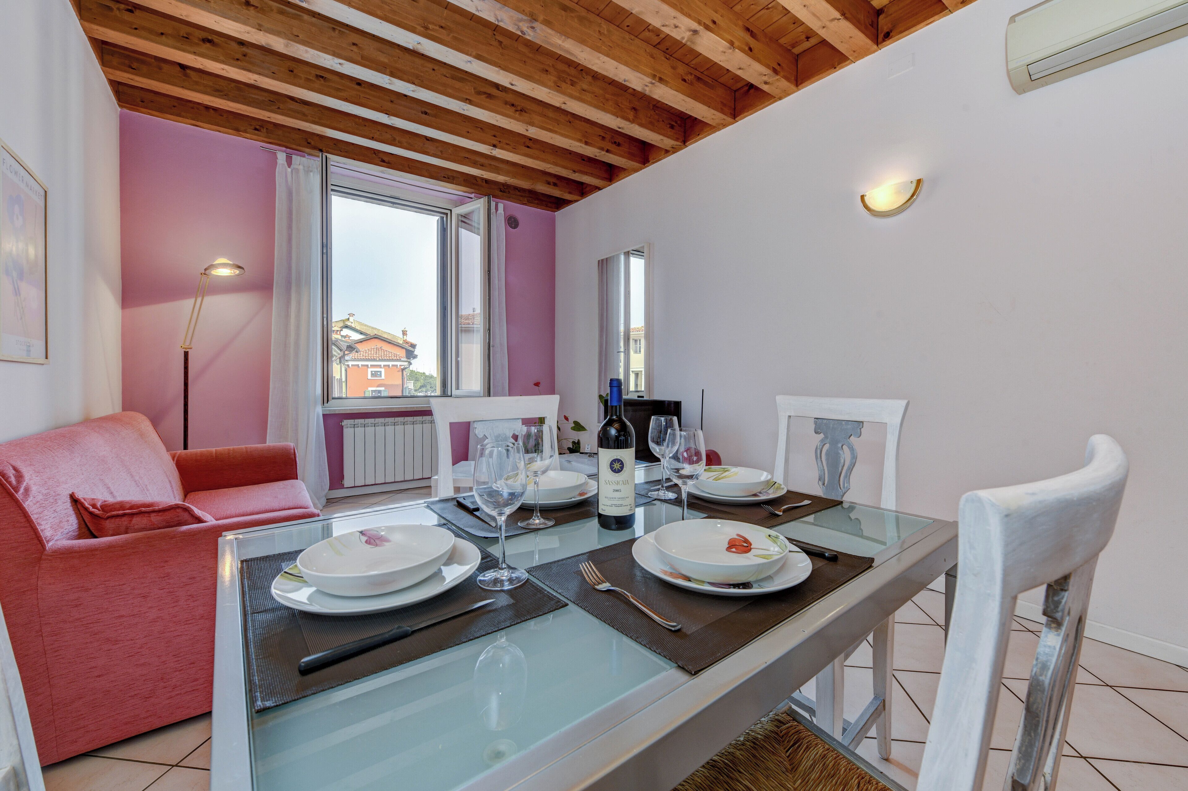 En matplats med ett glasbord för två personer, en rosa soffa och en vit stol.