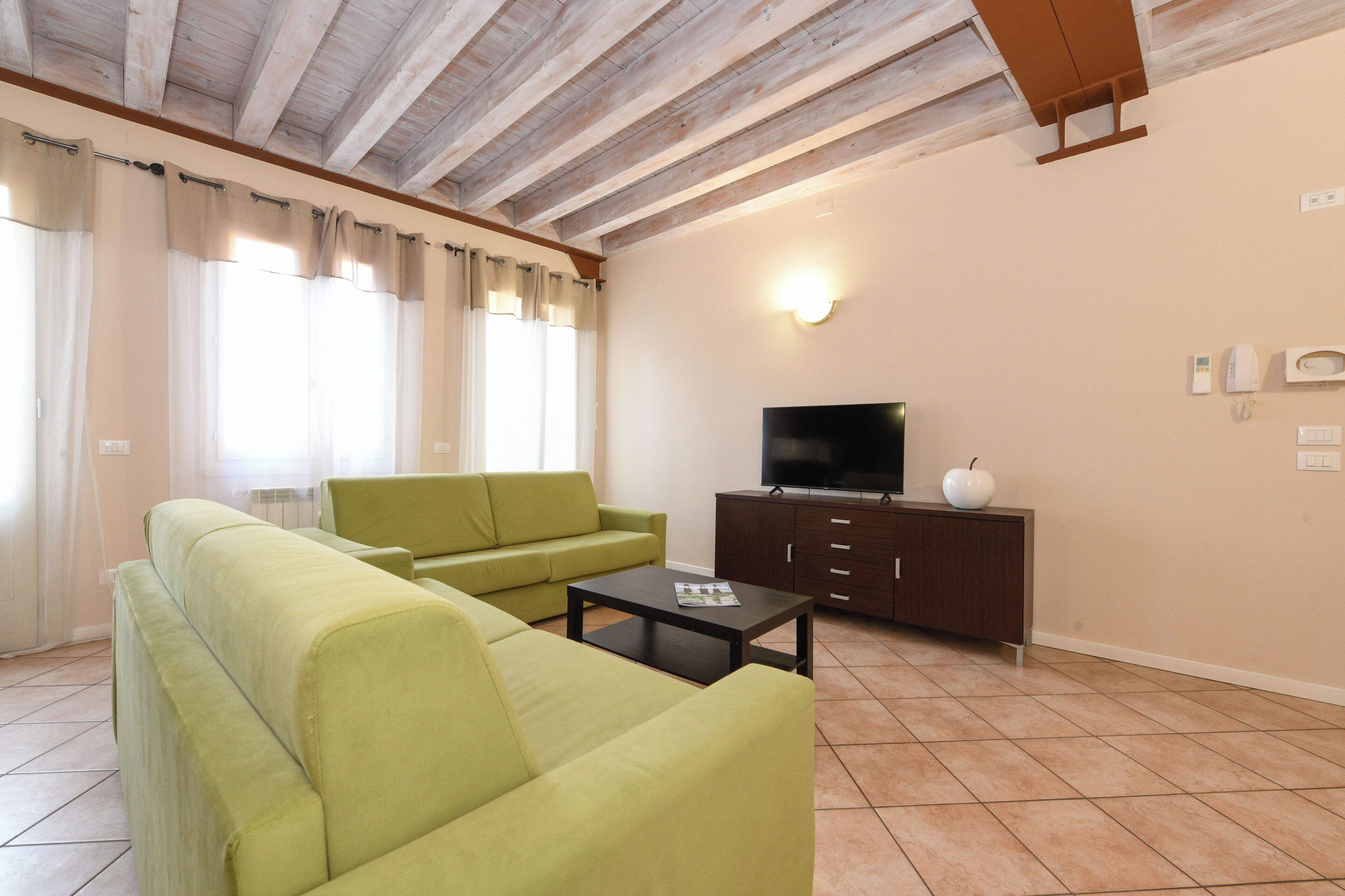 Una sala de estar con un sofá verde, una mesa de centro, un televisor sobre un mueble de madera y una ventana con cortinas.