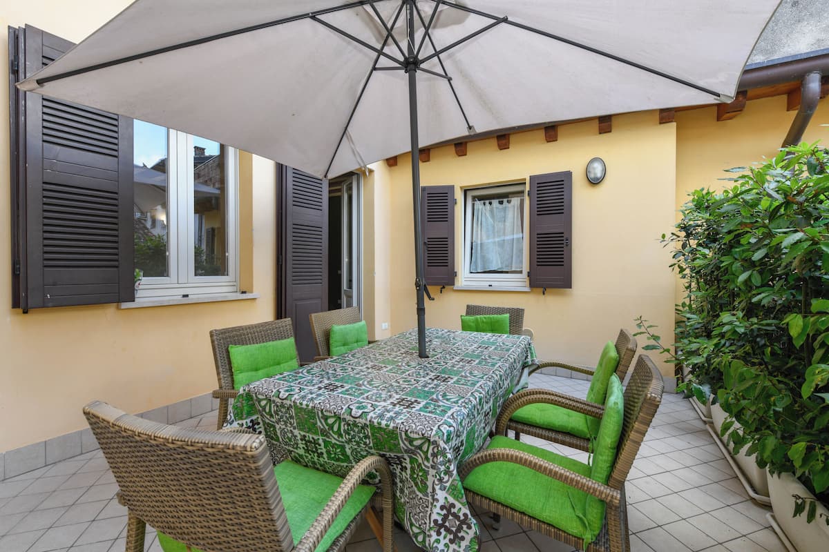 Eine Terrasse im Freien mit Tisch, Stühlen, einem großen Sonnenschirm und einem Blumentopf.