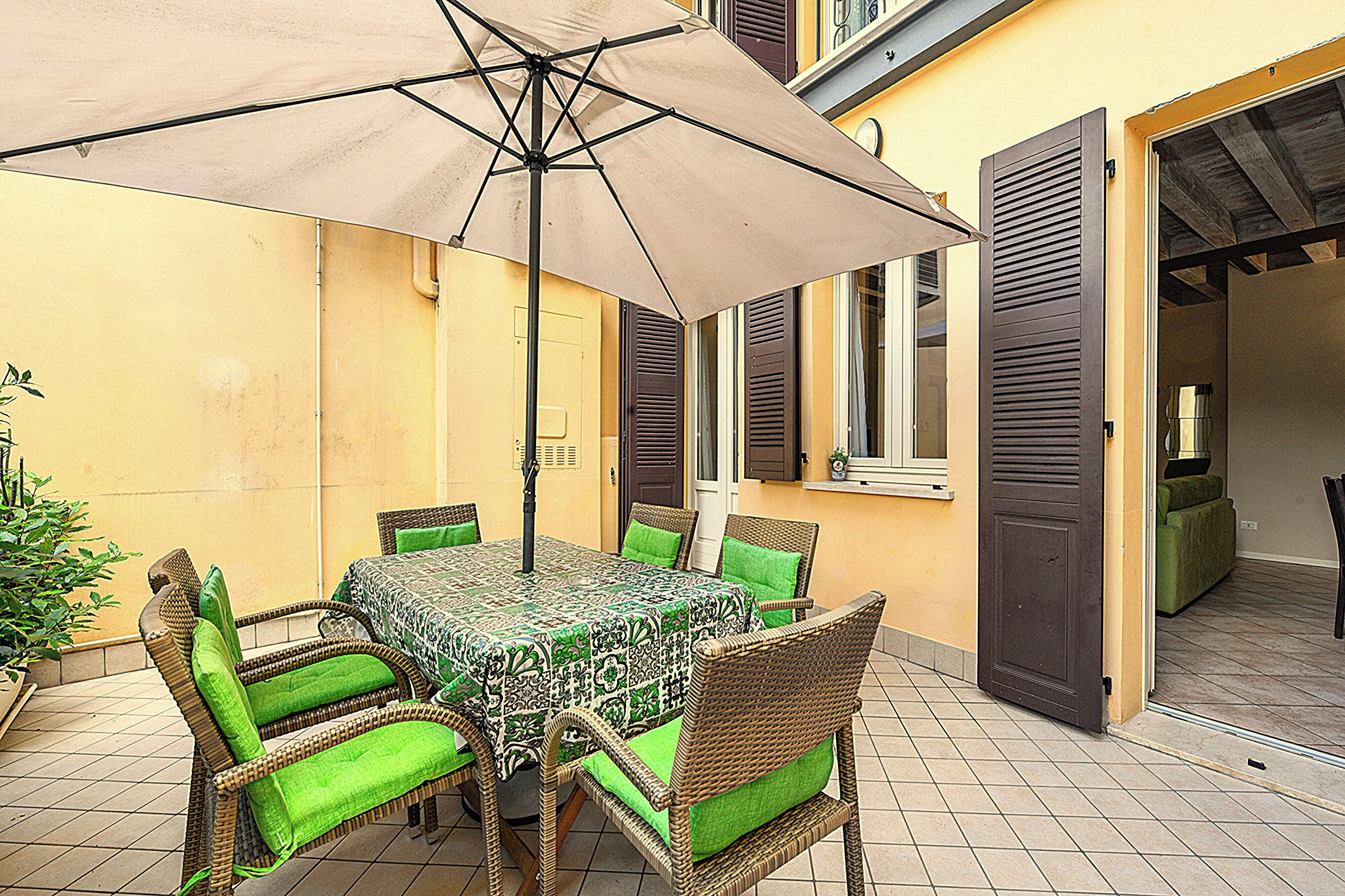 Une terrasse extérieure avec une table et des chaises, un parasol et une porte donnant sur un espace intérieur.