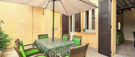 Une terrasse extérieure avec une table et des chaises, un parasol et une porte donnant sur un espace intérieur.
