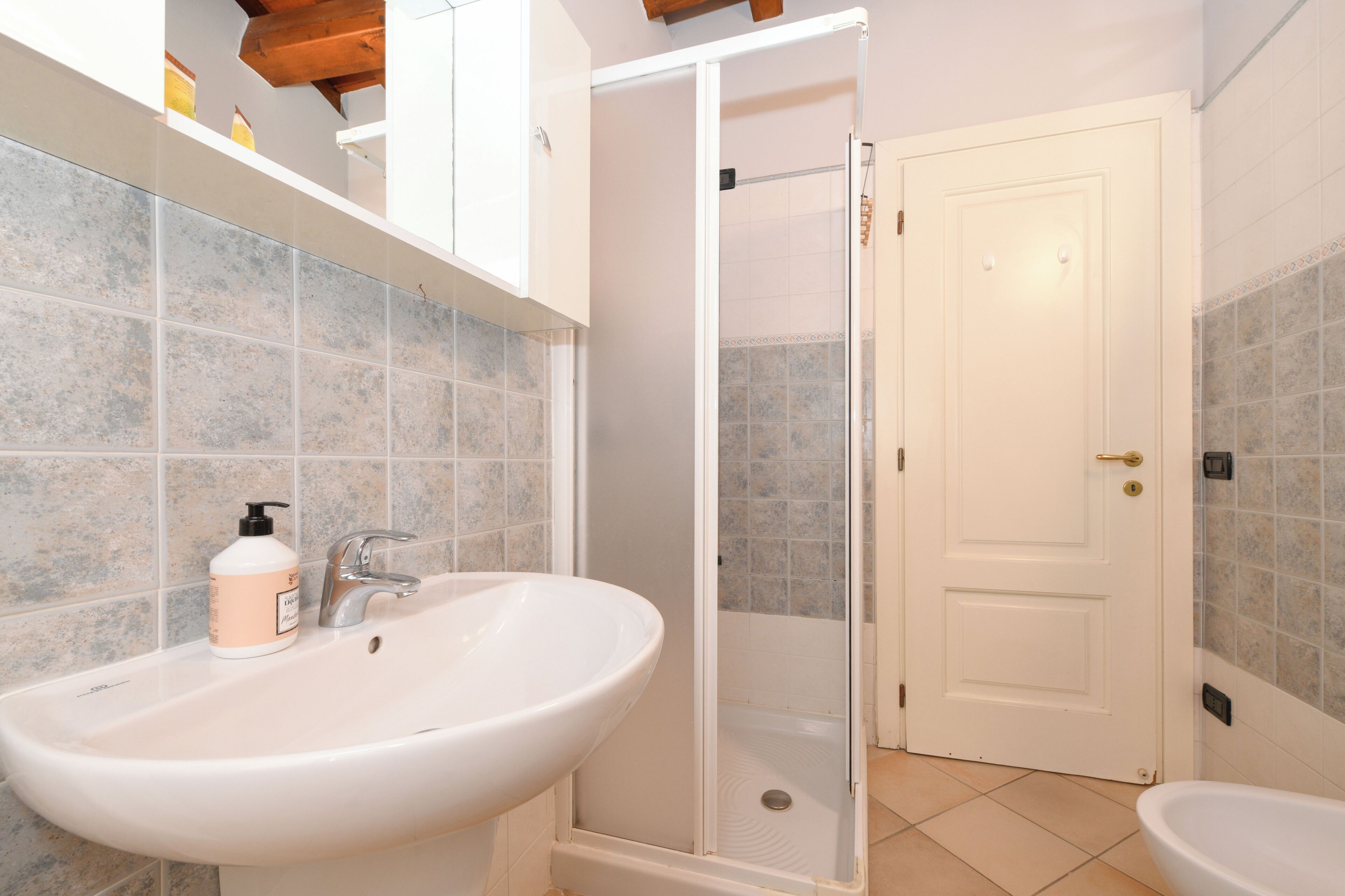 Un baño con un lavamanos blanco, cabina de ducha y una puerta blanca.