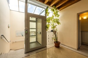A modern elevator with a glass door, a potted plant, and a view of the sky through the ceiling. - Flowers Apartments (Desenzano del Garda)