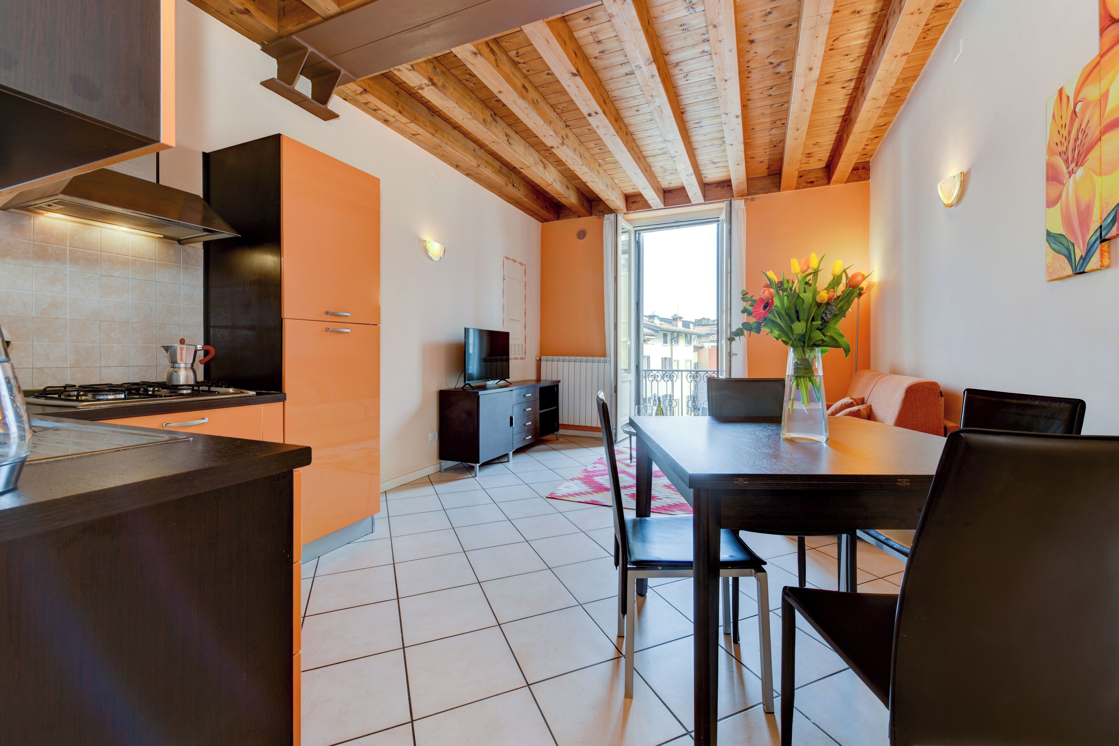 A modern kitchen with a gas stove, a built-in oven, and a microwave. There is a dining area with a table and chairs, and a large window providing a view of the city.