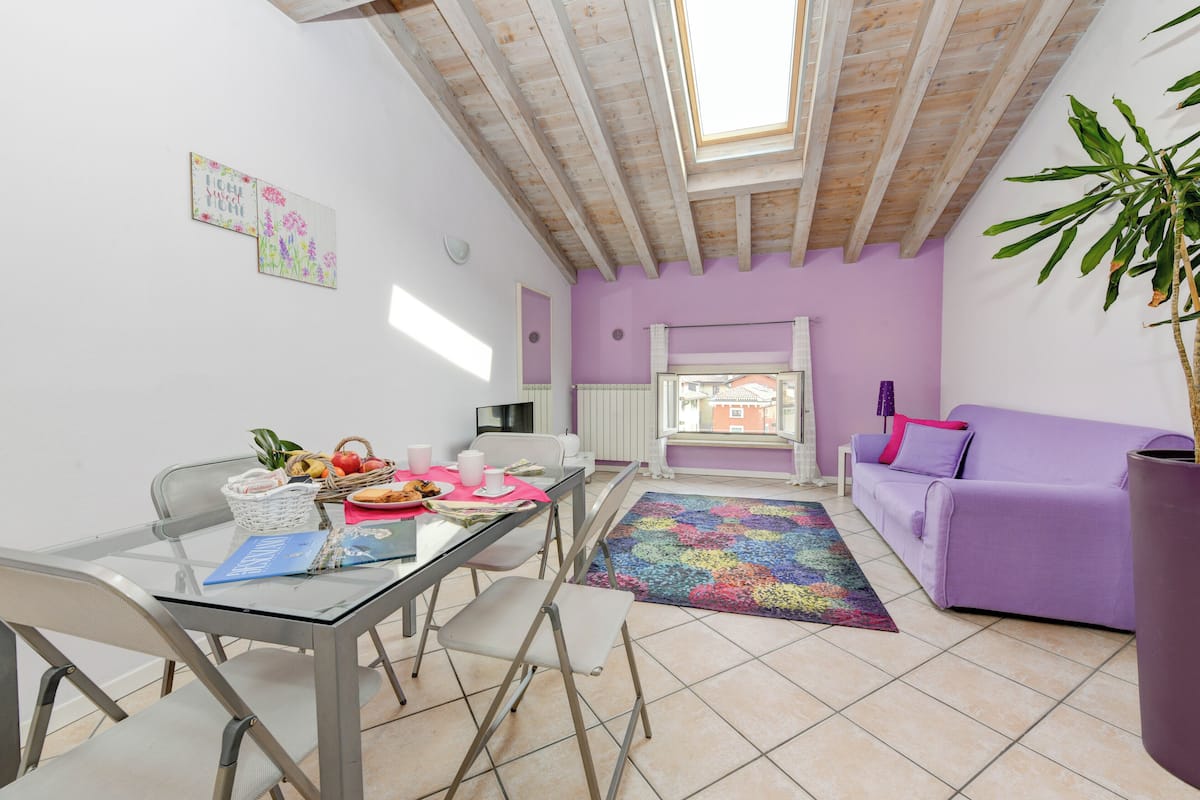 Ein Essbereich mit einem Glastisch, Stühlen und einem violetten Sofa.