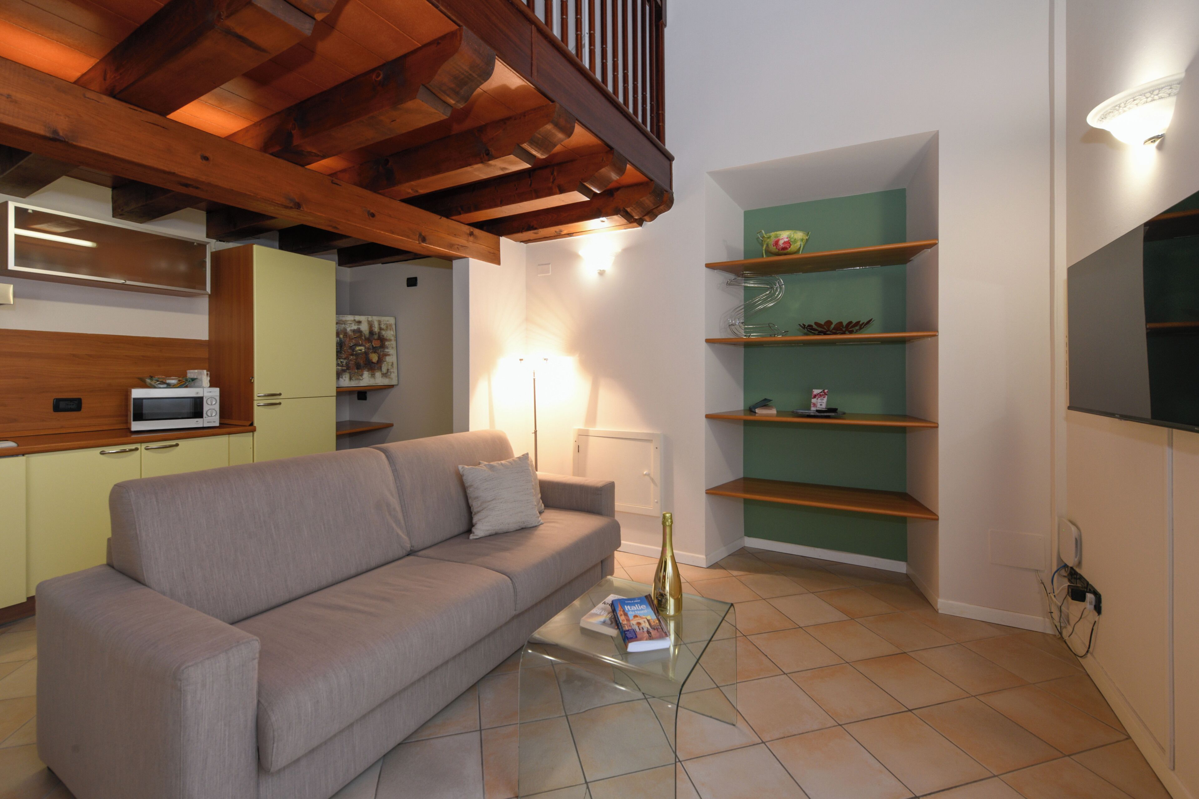 A living room with a sofa, a glass coffee table, a microwave, a green shelving unit, and a staircase.