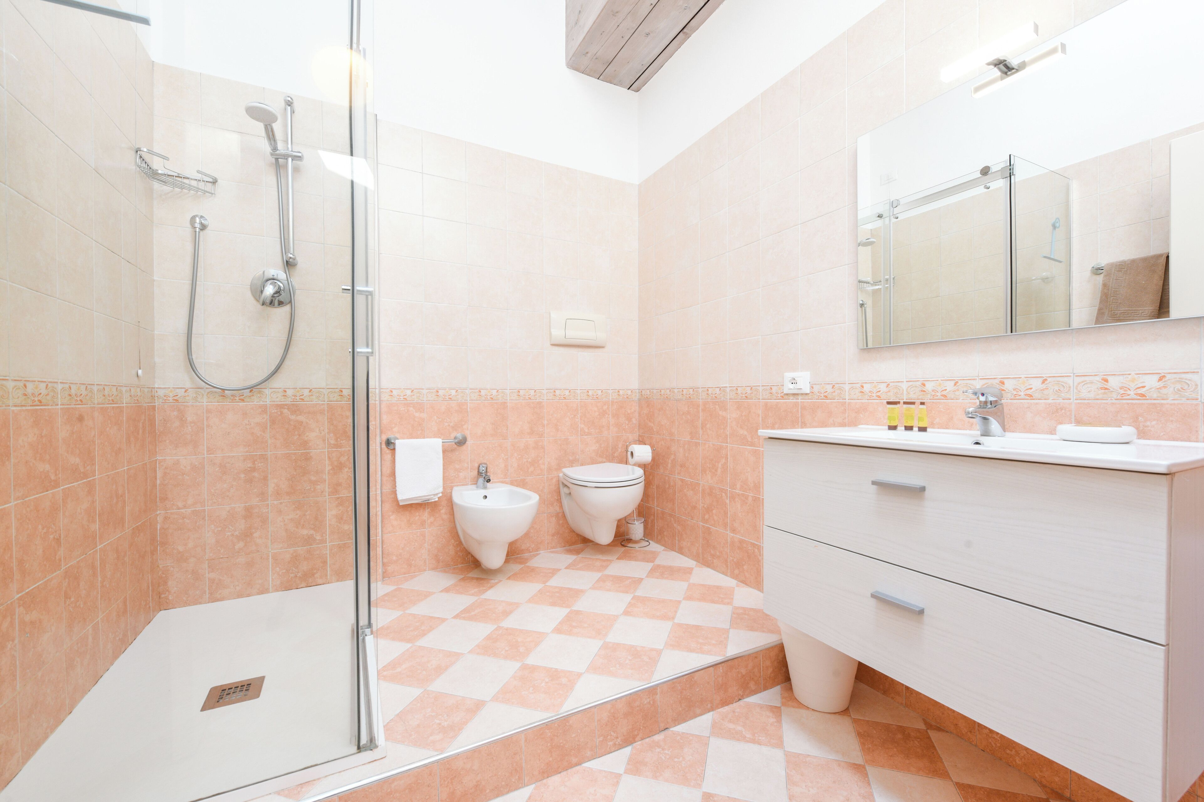A bathroom with a glass shower enclosure, a bidet, a toilet, and a vanity with drawers.