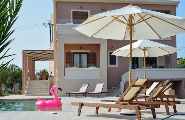 A pool area with lounge chairs, a flamingo float, and umbrellas.