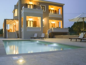 A modern two-story house with a swimming pool, outdoor seating, and a well-lit entrance.