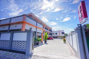 A modern building with a covered walkway, potted plants, and a red car parked in front. - OYO 1680 Hanna Residence (Manado)