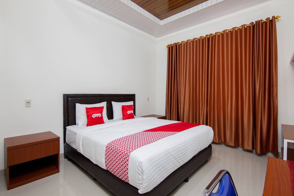 A hotel room with a bed, a nightstand, a desk, and a window with curtains.