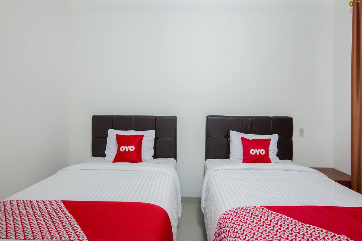 Two single beds with dark headboards, white bedding, and red pillows with the word "OYO" on them.