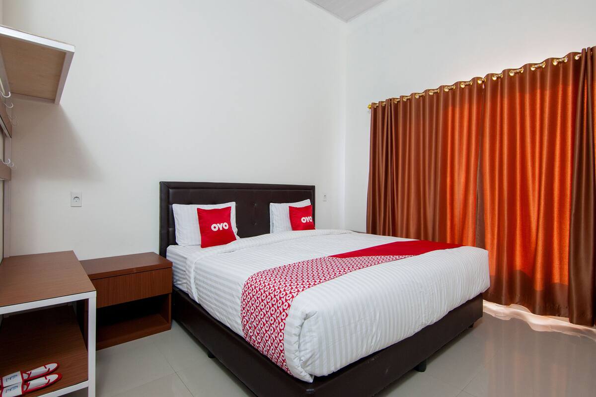 A neatly made bed with a white and red bedspread, two pillows with "OYO" branding, and a brown headboard.