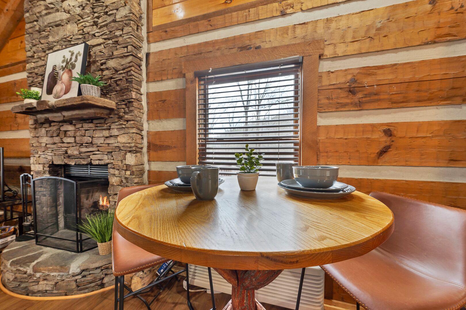 Interior acogedor de una cabaña de troncos con chimenea de piedra, una mesa redonda de madera y sillas de cuero.
