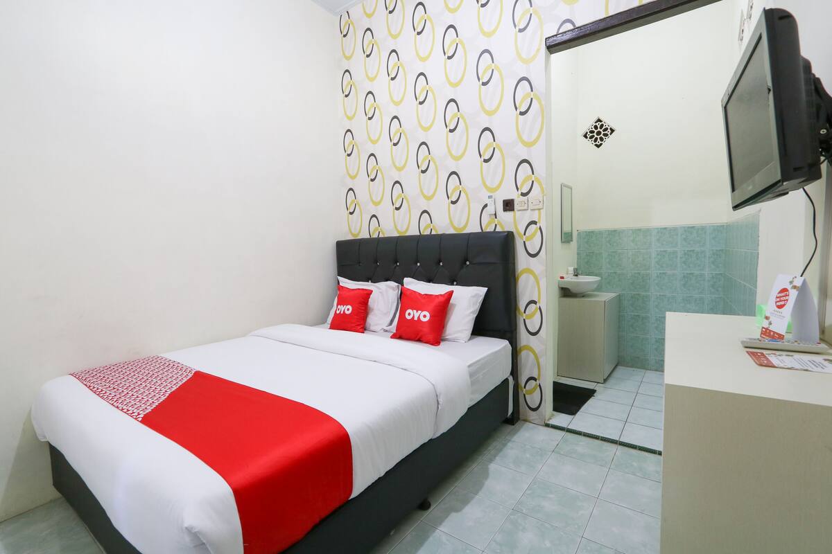 A hotel room with a bed, a bedside table, a TV, and a bathroom visible through an open door.